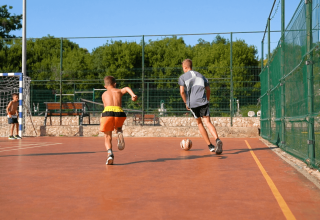 Kids play football on an outdoor court surrounded by greenery at Camping Krk in Primorje-Gorski Kotar, Croatia.