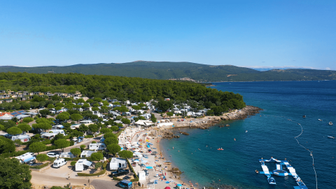 Vista aérea del Camping Krk en Croacia con su playa, caravanas y el azul mar Adriático al fondo.
