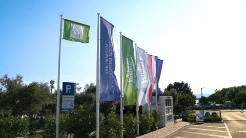 Flag i Camping Krk feriepark i Primorje-Gorski Kotar, Kroatien, med skilte og parkeringsområde i baggrunden.