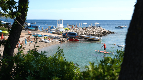 Vista de la playa en Camping Krk con personas, botes y sombrillas en Primorje-Gorski Kotar, Croacia.
