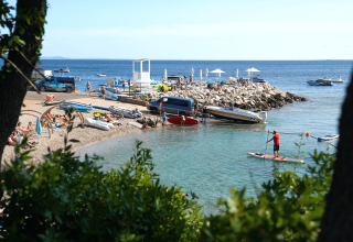 Strandscene med mennesker, både og parasoller på Camping Krk, en feriepark i Primorje-Gorski Kotar, Kroatien.