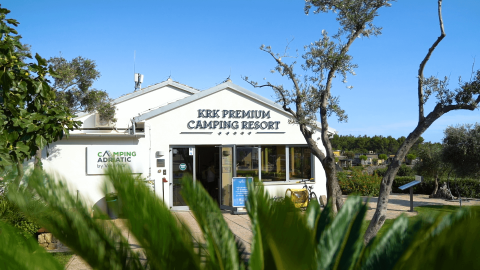 Entrada al KRK Premium Camping Resort en Croacia, rodeada de plantas verdes y cielo azul claro.
