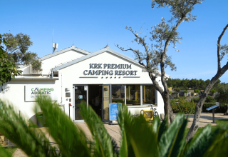 Ingresso del KRK Premium Camping Resort in Croazia, circondato da piante verdi e cielo azzurro.