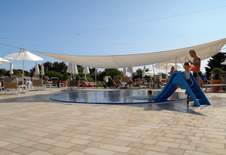 Piscina per bambini con scivolo blu e lettini sotto ombrelloni bianchi al Camping Krk, Croazia.