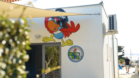 Murale colorato di pappagallo e insegna Margo Baby su un edificio bianco al Camping Krk in Croazia.