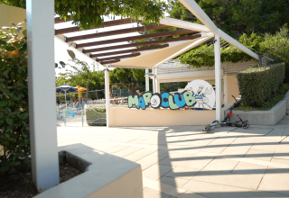 Ingang van de kinderclub bij Camping Krk, Kroatië, met een step en schaduwrijke buitenzitruimte.