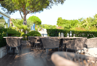 Zona pranzo all'aperto al Camping Krk con sedie intrecciate e verde rigoglioso in Croazia d'estate.