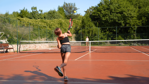 Dos niñas juegan al tenis en una pista exterior en Camping Krk, rodeadas de árboles en Croacia.