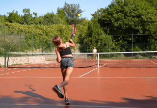 To piger spiller tennis på en udendørs bane omgivet af grønt, sandsynligvis i Camping Krk, Kroatien.