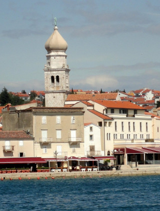Vista costera de Krk en Croacia con su icónica torre campanario y edificios de techo rojo junto al mar.