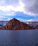 Puente que cruza una colina rocosa en el agua bajo un cielo espectacular, cerca de parque de glamping.