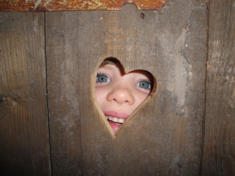 Un niño mira a través de un agujero en forma de corazón en una pared de madera en Feather Down Hohenwarter Seehof.