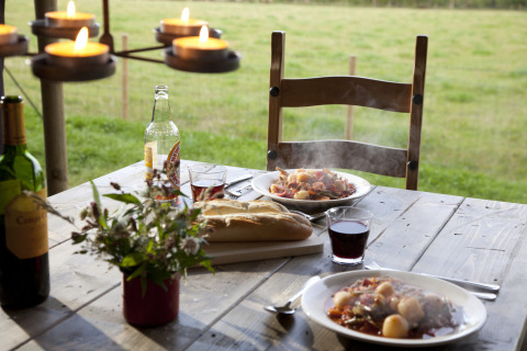 Outdoor meal on wooden table with wine, bread, hot stew, and candles, overlooking fields in Germany.