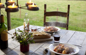 Buiteneten op houten tafel met wijn, brood, stoofpot en kaarsen, zicht op groene velden in Duitsland.