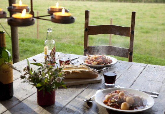 Repas en plein air sur table en bois avec vin, pain, ragoût chaud et bougies, vue sur la campagne allemande.