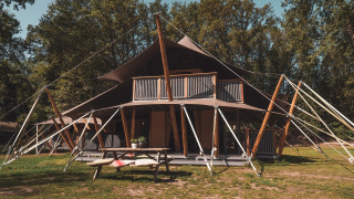 Tienda safari Kings Lodge + Hot Tub en Sandberghe, Países Bajos, rodeada de árboles y césped verde.