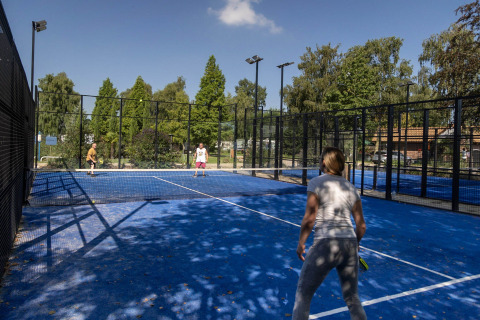 Vakantiegangers spelen padel op het blauwe buitenveld met omheining en bomen bij Camping Papillon in Limburg.