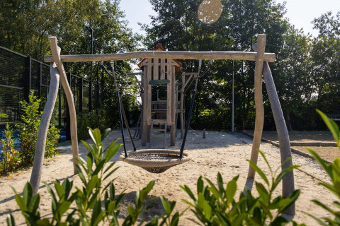 Parque infantil con columpios y tobogán en el Camping Papillon en Limburgo belga, rodeado de árboles.
