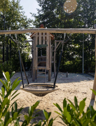 Parque infantil con columpios y tobogán en el Camping Papillon en Limburgo belga, rodeado de árboles.