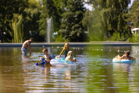 Bambini giocano con ciambelle e pistole d’acqua nell’acqua bassa al Camping Papillon in Belgio.