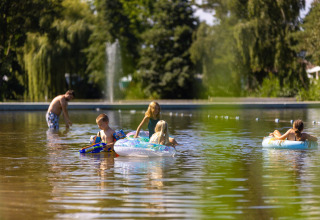 Bambini giocano con ciambelle e pistole d’acqua nell’acqua bassa al Camping Papillon in Belgio.