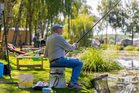 Un uomo anziano pesca accanto al lago presso il Camping Papillon, parco vacanze nel Limburgo belga, Belgio.