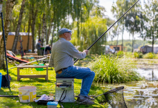 Un uomo anziano pesca accanto al lago presso il Camping Papillon, parco vacanze nel Limburgo belga, Belgio.