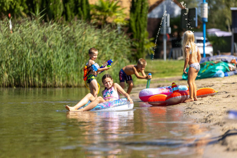 Niños juegan con pistolas de agua y flotadores en la orilla del lago en Camping Papillon, Limburgo belga.