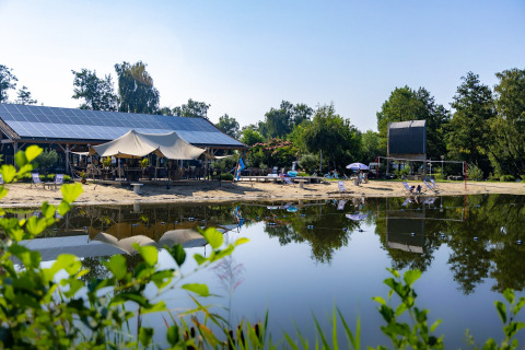 Zonnig strand aan meer, ligstoelen en zonnepanelenpaviljoen bij Kinrooi in Belgisch Limburg, België.