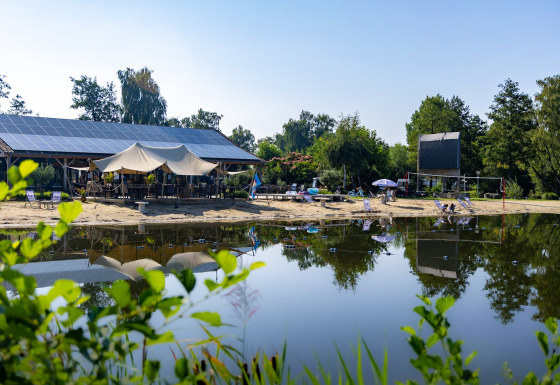 Ein ruhiger See mit Sandstrand, Liegestühlen und Solarzellenpavillon bei Kinrooi, Limburg, Belgien.