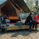 Dos ciclistas con ropa deportiva se sientan frente a una tienda Safari tent XS con bicicletas y mochilas.