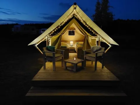 Tienda safari XS en Camp Kyllburg, Alemania, iluminada por la noche con luces y asientos acogedores afuera.