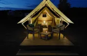 Tienda safari XS en Camp Kyllburg, Alemania, iluminada por la noche con luces y asientos acogedores afuera.