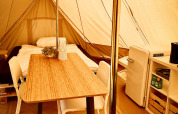 Interior de una tienda tipi en Camp Kyllburg, Alemania, con cama, mesa, sillas, nevera y estantería.