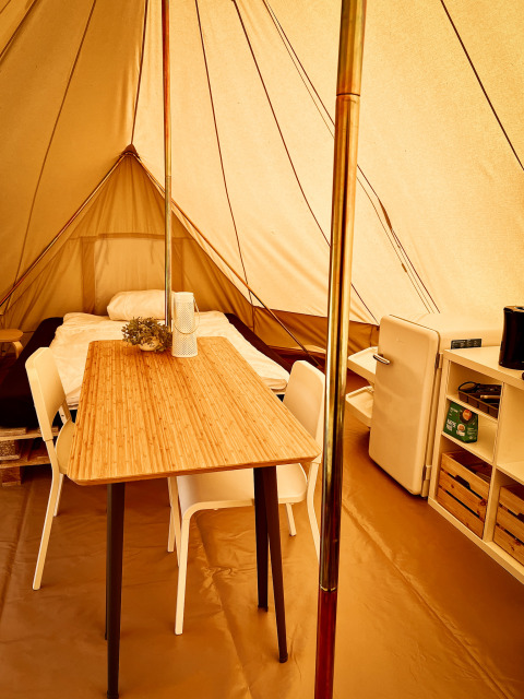 Intérieur d’une tente tipi au Camp Kyllburg, Allemagne, avec lit, table, chaises, frigo et étagère.