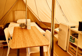 Interno di una tenda tipì al Camp Kyllburg, Germania, con letto, tavolo, sedie, frigorifero e scaffale.