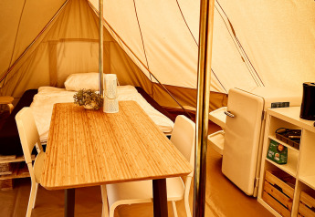 Interno di una tenda tipì al Camp Kyllburg, Germania, con letto, tavolo, sedie, frigorifero e scaffale.