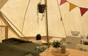 Interior de una tienda Tipi con cama, mesa de comedor, frigorífico, cojines y decoraciones coloridas.