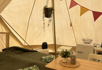Indretning af en Tipi-telt med dobbeltseng, spisebord, køleskab og hyggelig dekoration indenfor.