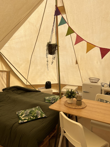 Interior de una tienda Tipi con cama, mesa de comedor, frigorífico, cojines y decoraciones coloridas.