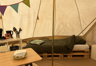 Interior de una tienda tipi en Camp Kyllburg, Alemania, con cama sobre palets, mesa y banderines de colores.