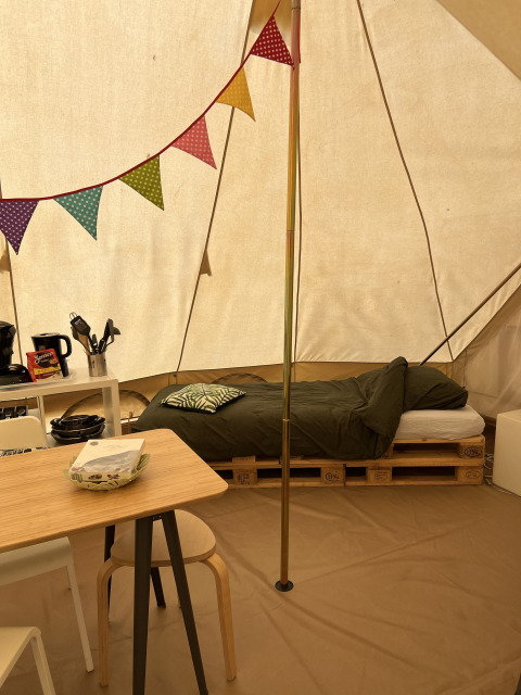 Innenraum eines Tipi-Zeltes mit Bett auf Paletten, Tisch und Girlande, Camp Kyllburg, Deutschland.