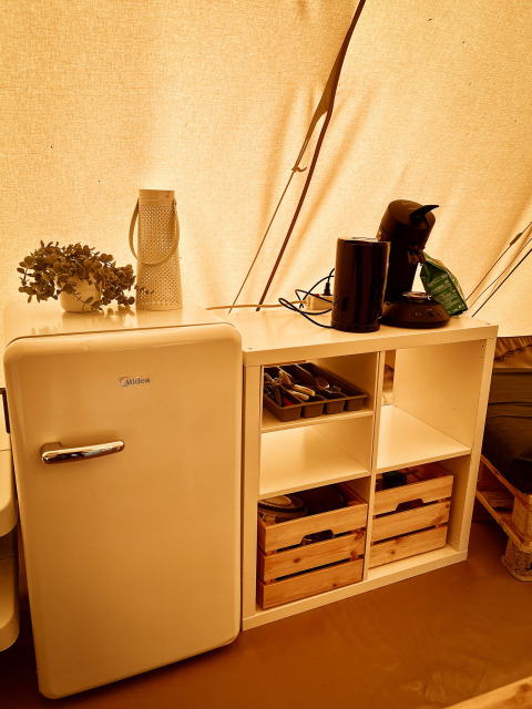 Ausstattung im Tipi-Zelt bei Camp Kyllburg in Deutschland mit Kühlschrank, Utensilien und Kaffeemaschine.