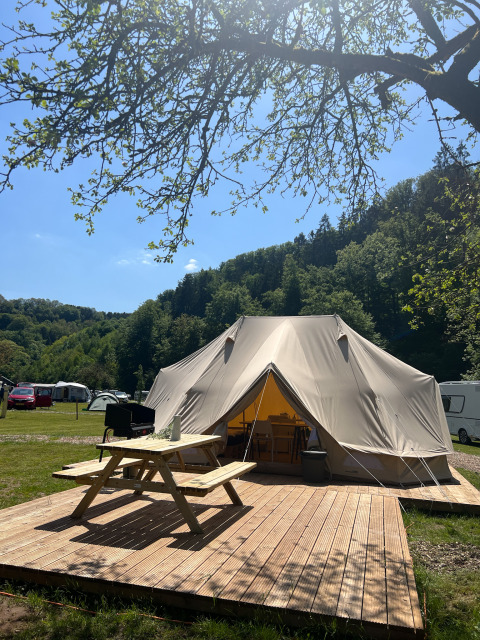 Gran tienda tipi en una plataforma de madera con mesa de picnic, rodeada de naturaleza y colinas verdes.