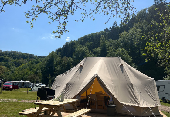 Gran tienda tipi en una plataforma de madera con mesa de picnic, rodeada de naturaleza y colinas verdes.
