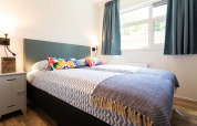 Dormitorio luminoso con almohadas coloridas, gran ventana y decoración moderna en una tiny house en Holiday Park Gelloo.