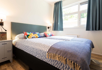 Lyst soveværelse med farverige puder, stort vindue og moderne indretning i en tiny house ved Holiday Park Gelloo.