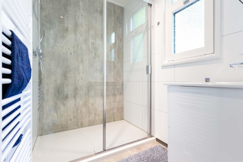 Ducha moderna con mampara de vidrio, radiador toallero y ventana en el Special Wellness Module, Holiday Park Gelloo, Países Bajos.