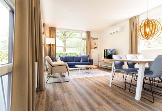 Sala luminosa y moderna con mesa de comedor, sofá azul y lámpara de diseño en Holiday Park Gelloo, NL.