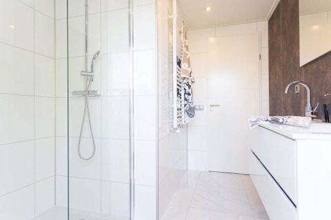 Baño moderno con ducha, azulejos blancos y lavabo en Collosseo Wellness de Résidence Valkenburg, Países Bajos.